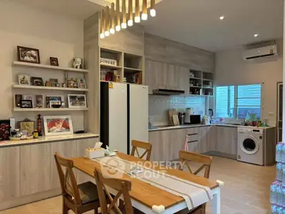 Modern kitchen with wooden cabinets, dining table, and washing machine, featuring open layout and stylish lighting.