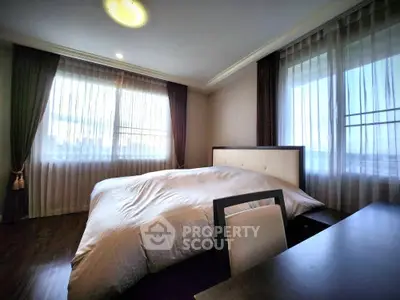 Spacious bedroom with large windows and elegant curtains, offering a serene and cozy atmosphere.