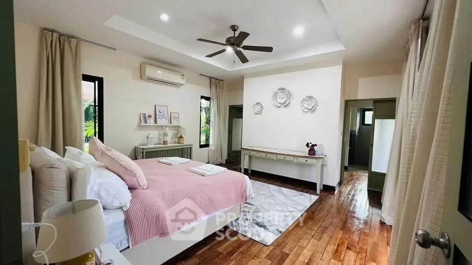 Spacious bedroom with elegant decor and hardwood floors, featuring a ceiling fan and natural light.