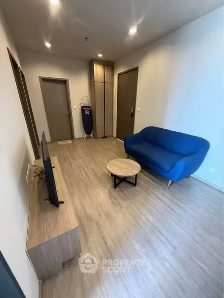 Modern living room with blue sofa and flat-screen TV, featuring wooden flooring and minimalist decor.