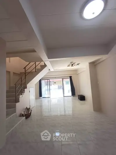 Spacious open-plan living area with modern staircase and large windows for natural light.