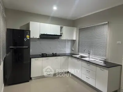 Modern kitchen with sleek black and white cabinetry, gas stove, and large fridge.