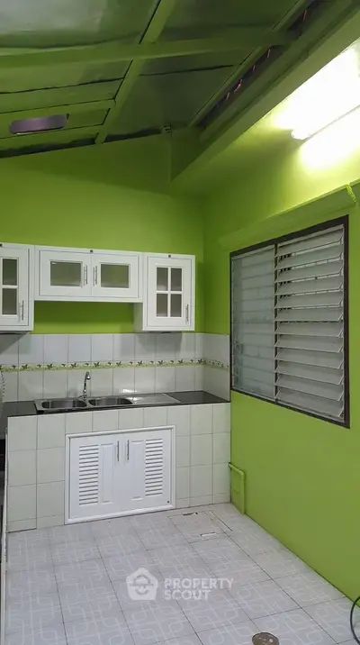 Bright green kitchen with white cabinets and tiled floor, featuring a modern sink and large window.