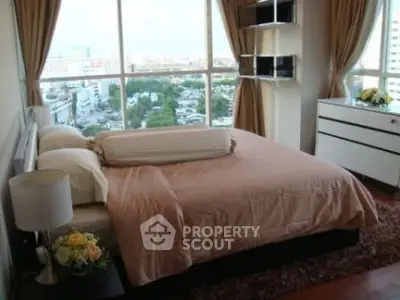 Spacious bedroom with large windows offering a stunning city view, elegant decor, and ample natural light.