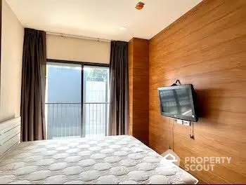 Cozy bedroom with large windows and balcony access, featuring a wall-mounted TV and rich wooden paneling for a modern yet warm ambiance.