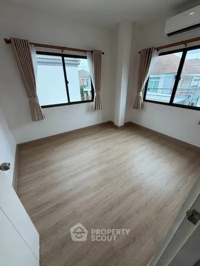 Spacious bedroom with large windows and wooden flooring in a modern home.