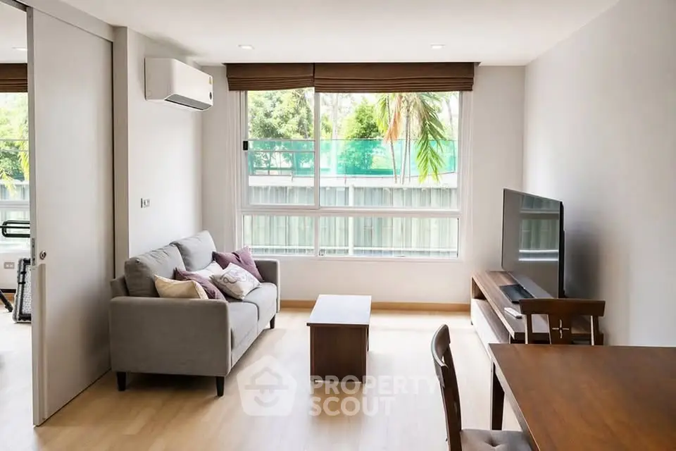 Modern living room with large window, cozy sofa, and sleek TV setup in a bright apartment.