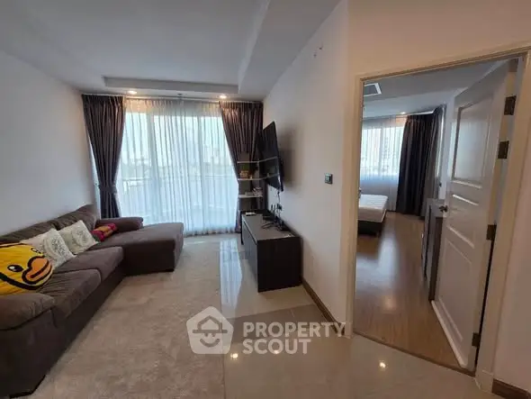 Modern living room with cozy sofa and TV, leading to a bright bedroom.