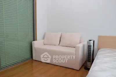 Cozy bedroom with a small sofa and modern fan, featuring wooden flooring and blinds.