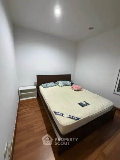 Cozy bedroom with wooden flooring and minimalist design, featuring a comfortable bed and soft lighting.