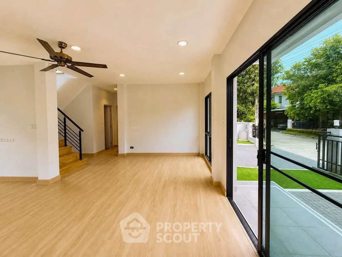 Spacious living room with wooden flooring and large sliding glass doors opening to a garden view.