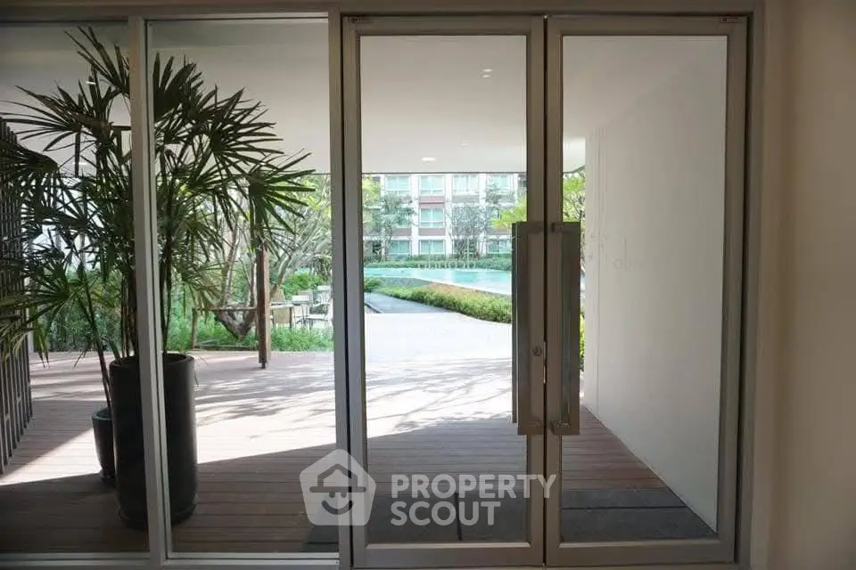 Modern building entrance with glass doors and lush greenery view.