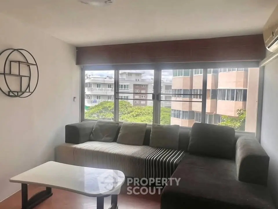 Modern living room with large windows and stylish sectional sofa in urban apartment.