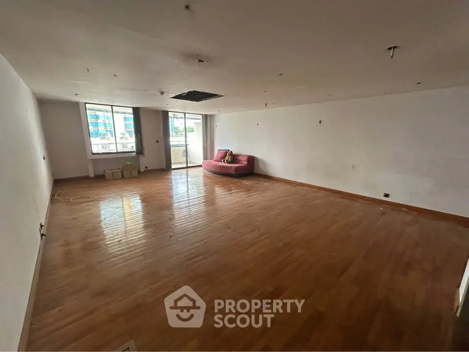 Spacious unfurnished room with wooden flooring and large window, ideal for customization.