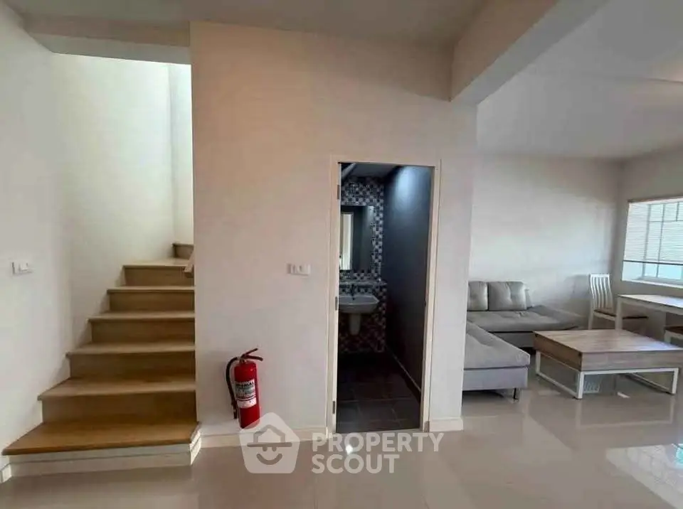 Modern living room with staircase and open layout, featuring sleek furniture and a cozy atmosphere.