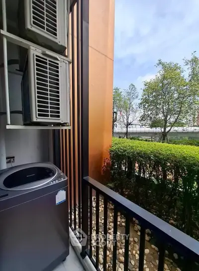 Charming balcony with lush garden view and modern air conditioning unit, perfect for relaxation.