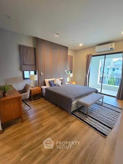 Spacious modern bedroom with elegant decor and balcony access, featuring wooden flooring and stylish furnishings.