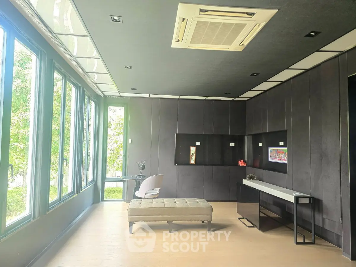 Modern living room with large windows and sleek black paneling, featuring stylish furniture and natural light.