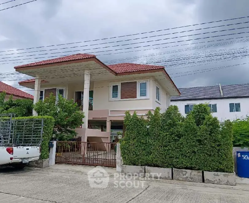 Charming two-story house with lush greenery and gated entrance in a serene neighborhood.