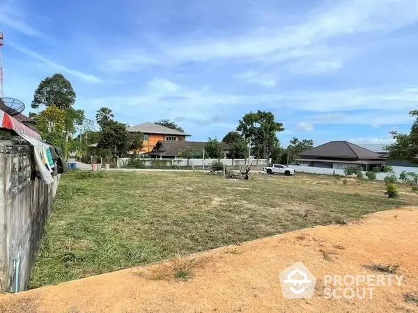 Expansive vacant land with clear skies and potential for development, surrounded by a peaceful residential area.