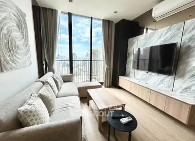 Modern living room with large windows and city view, featuring stylish decor and a wall-mounted TV.