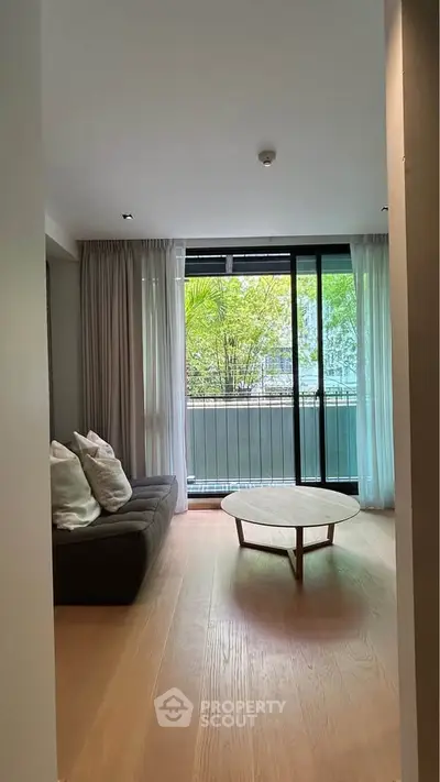 Spacious living room with large windows and a view of greenery, featuring a modern sofa and round coffee table.