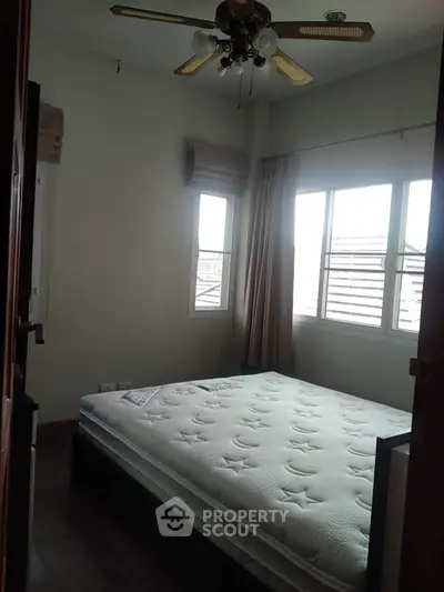 Spacious bedroom with large windows, natural light, and a ceiling fan, perfect for comfortable living and relaxation.