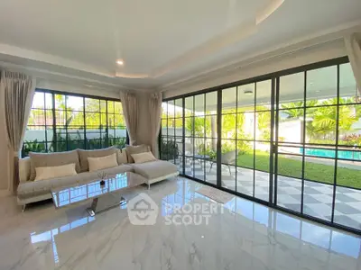 Luxurious living room with large windows overlooking a lush garden and pool, featuring elegant marble flooring and modern decor.