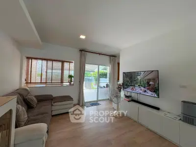Spacious living room with modern decor and large TV, featuring a cozy sofa and natural light from large windows.