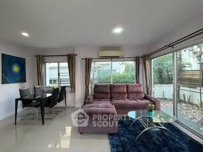 Modern living room with plush sofa and dining area, featuring large windows and garden view.