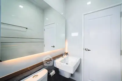 Modern bathroom with sleek sink and large mirror, featuring elegant lighting and minimalist design.