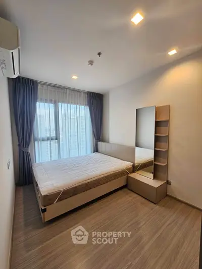 Modern bedroom with large window and sleek furnishings in a contemporary apartment.