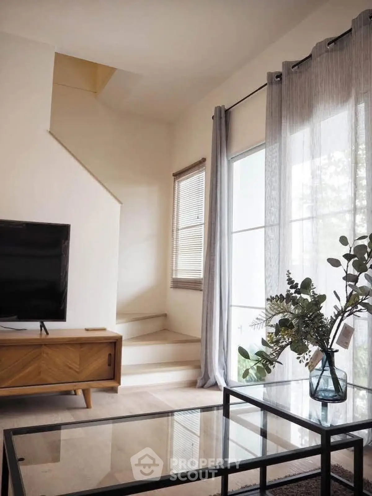 Stylish living room with modern decor, large window, and elegant staircase in a bright home.