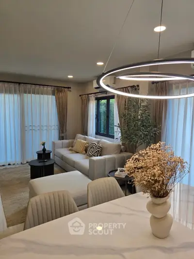 Elegant living room with modern decor, featuring a cozy sofa, stylish lighting, and large windows with sheer curtains.