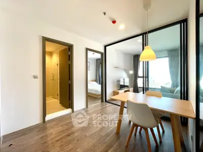 Modern apartment interior with open layout, featuring dining area and view into bedroom.