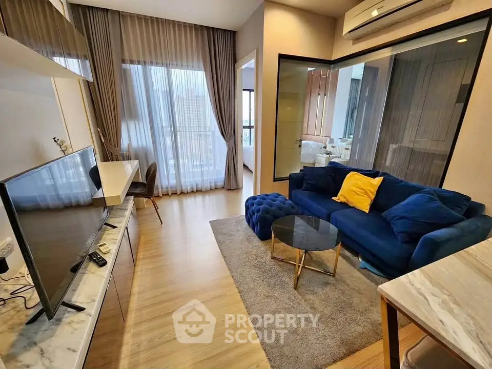 Modern living room with blue sofa, TV, and large windows in stylish apartment.