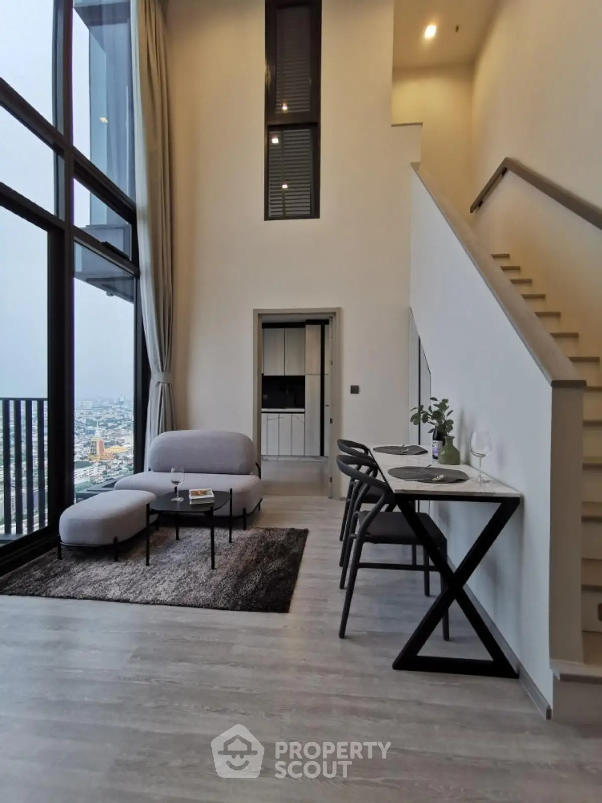 Modern duplex apartment with high ceilings and city view, featuring stylish furniture and elegant staircase.