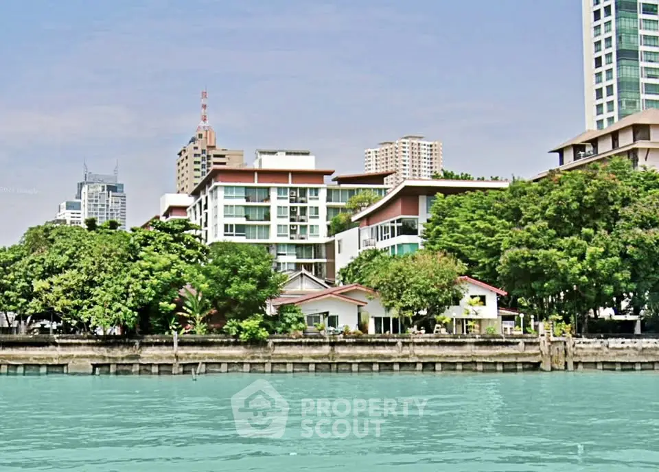 Stunning waterfront view of modern residential buildings with lush greenery and serene river setting.