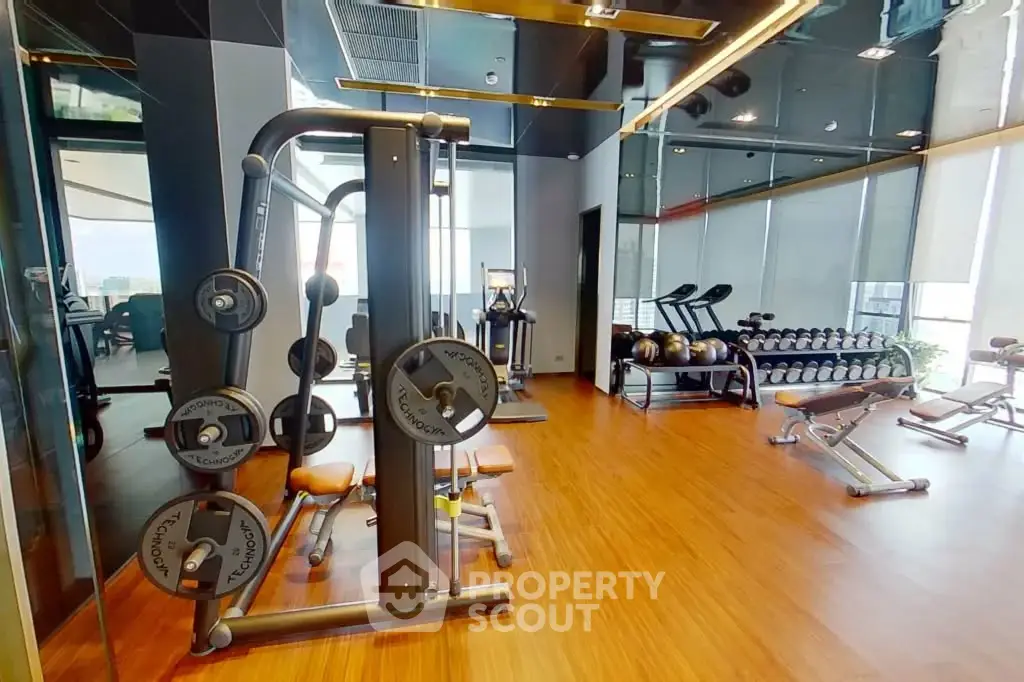 Modern gym with state-of-the-art equipment and wooden flooring in luxury apartment building.