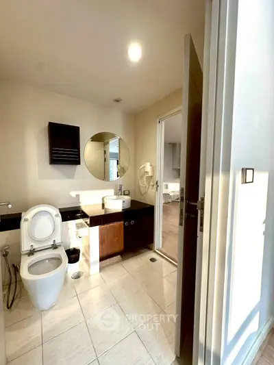 Modern bathroom with round mirror and open door to living area