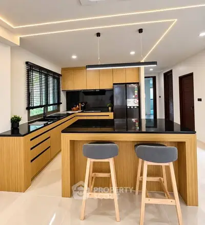 Modern kitchen with sleek wooden cabinetry and island seating, featuring contemporary lighting and appliances.