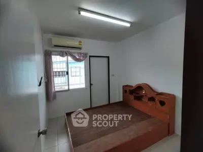 Cozy bedroom with wooden bed frame and air conditioning in a bright, minimalist space.