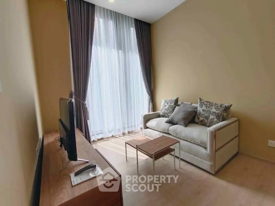Cozy living room with modern sofa and TV, featuring floor-to-ceiling windows and elegant curtains.