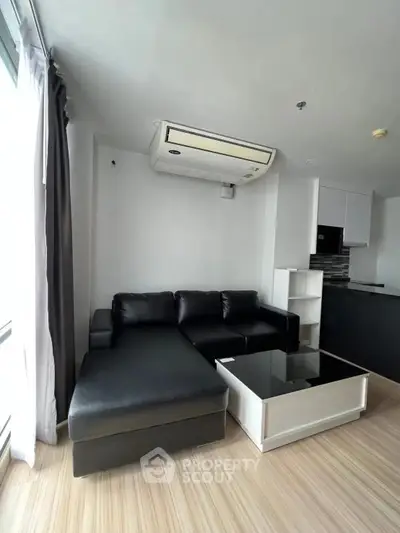Modern living room with black leather sofa and sleek kitchen in open layout apartment.