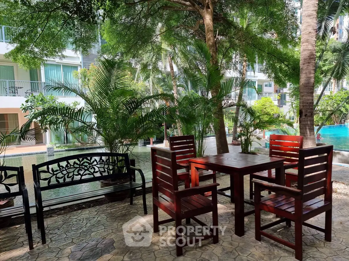 Charming outdoor seating area with lush greenery and pool view in a modern residential complex.