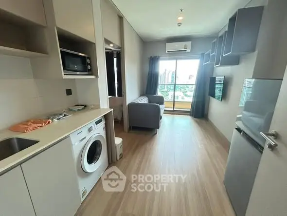 Modern apartment interior with open kitchen and living area, featuring washing machine and balcony view.
