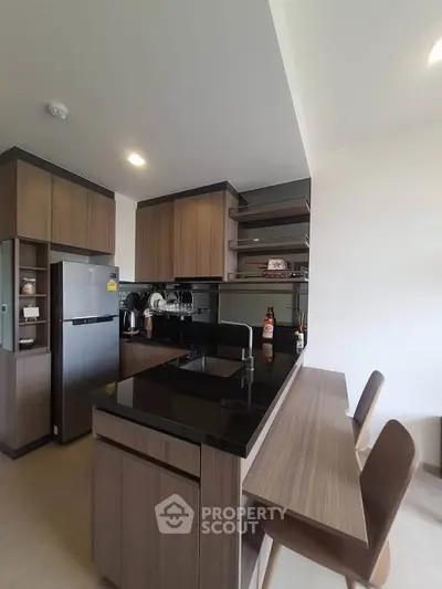 Modern kitchen with sleek wooden cabinets and black countertops, featuring a breakfast bar and stainless steel appliances.