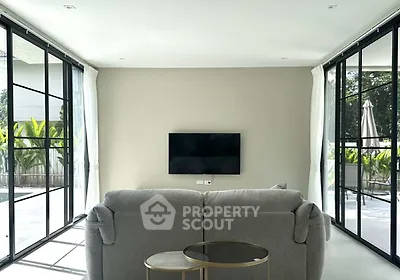 Modern living room with large windows and poolside view, featuring sleek furniture and minimalist design.