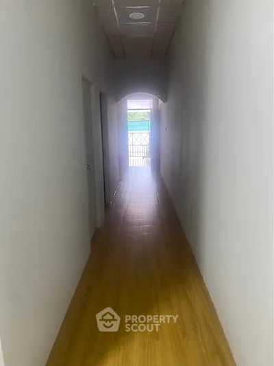 Long hallway with wooden flooring leading to a bright balcony view.