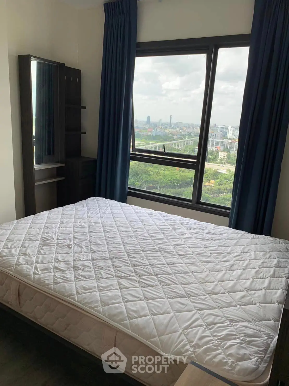 Spacious bedroom with large window offering stunning cityscape views, perfect for urban living.
